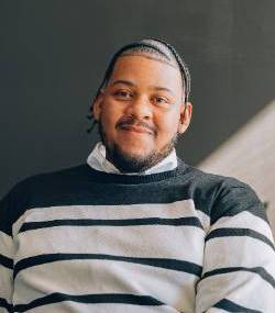 A headshot of Marquis wearing a striped sweater