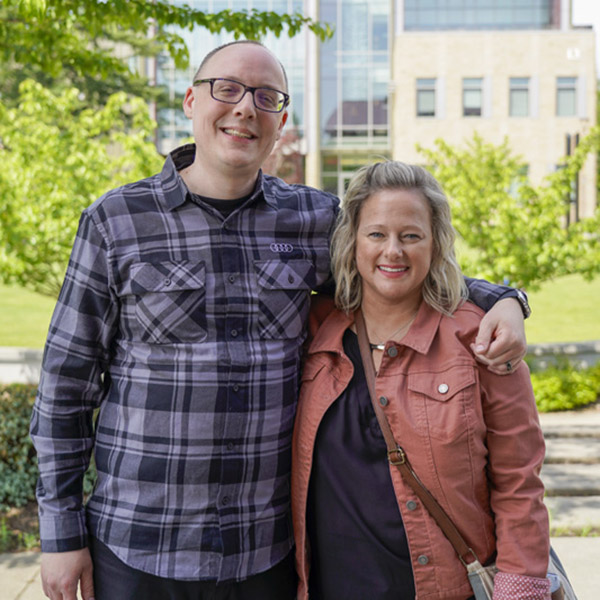 man in plaid shirt and glasses and woman in peach jacket smiling 