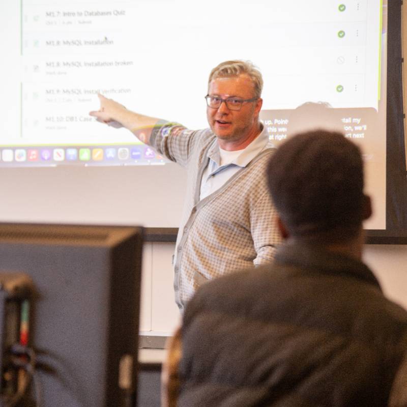 a professor pointing to a screen in a classroom