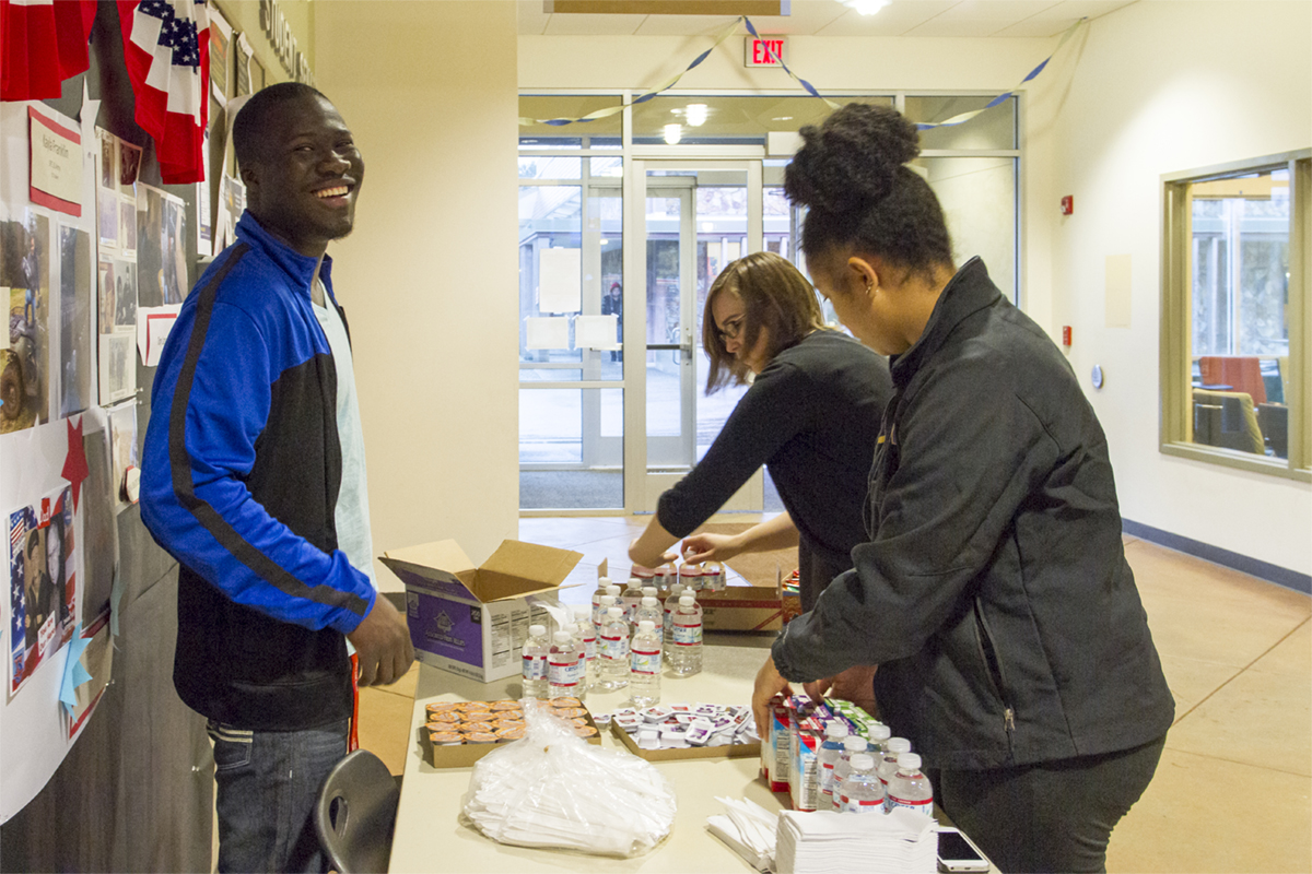 A smiling male student and two female students distribute snacks in the Student Center